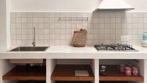 A kitchen with a white countertop, a sink, a gas stove, and wooden shelves below.