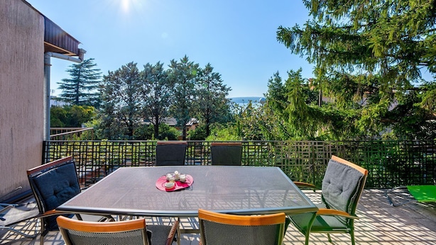 Eine Terrassengaststätte mit Tisch und Stühlen, umgeben von einem Metallzaun, mit Blick auf ein bewaldetes Gebiet.