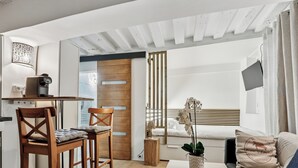 Ein moderner, gut beleuchteter Raum mit einem Holzespeisetisch, zwei Stühlen, einer Couch, einem kleinen Couchtisch und einem Bett mit Holz Kopfteil.