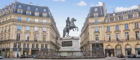 Stately equestrian statue stands proudly in the center of a spacious square, surrounded by two grand, multi-story buildings with ornate details.