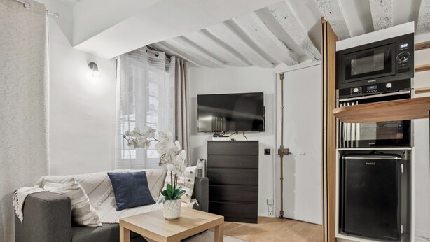 Ein modernes Wohnzimmer mit einem grauen Sofa, einem Holztisch und einem an der Wand befestigten Fernseher.