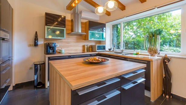 Een moderne keuken met een houten eiland, inbouwapparatuur en een groot raam met uitzicht op groen.