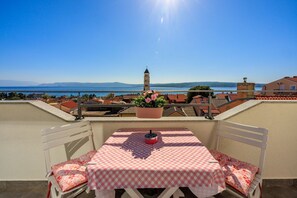 A terrace with a checkered table and chairs, overlooking a coastal town with a church and mountains in the distance. - Exquisite flat just 350 metres from the beach with stunning sea views, private parking, WiFi (Crikvenica)