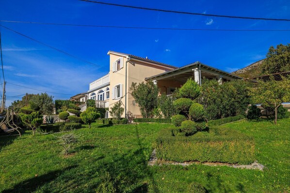 A two-story house with a balcony, surrounded by well-maintained gardens and trees.