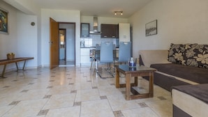 A modern living room with a sofa, a coffee table, and a dining area with chairs and a kitchen in the background. - Charming apartment only 300 meters to the beach with sea view, barbecue area - dog friendly (Crikvenica)