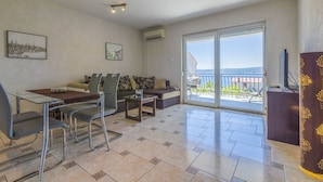 A modern living room with a dining area, large sliding glass doors to a balcony, and a flat-screen TV on a wooden cabinet. - Charming apartment only 300 meters to the beach with sea view, barbecue area - dog friendly (Crikvenica)