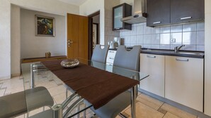 A modern kitchen with a dining area, featuring a glass table, metal chairs, and a built-in stove. - Charming apartment only 300 meters to the beach with sea view, barbecue area - dog friendly (Crikvenica)