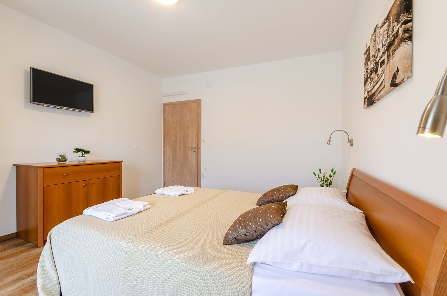 Une chambre d’hôtel bien rangée, avec un lit, une commode en bois, un téléviseur et une porte.