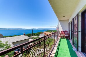 Un balcon avec vue sur la mer, un tapis vert et des chaises rouges.