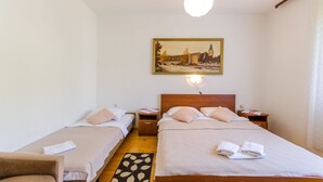 Camera d'albergo con due letti singoli, una testiera in legno, un quadro raffigurante un ponte, una lampada da comodino e un piccolo tavolo con lampada.