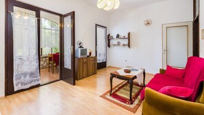 A living room with a wooden floor, a red sofa, a small table with a rug, a television on a wooden cabinet, and a hanging light fixture. - Nostalgic apartment only 500 meters to the beach with private terrace, sea view, barbecue (Dramalj)