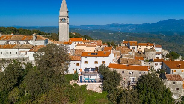 Un pittoresco villaggio costiero con una torre imponente, edifici con tetti in terracotta e una vegetazione rigogliosa.