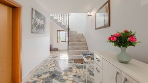 Un corridoio con pavimento in pietra, una porta in legno, una scala e un vaso con fiori.