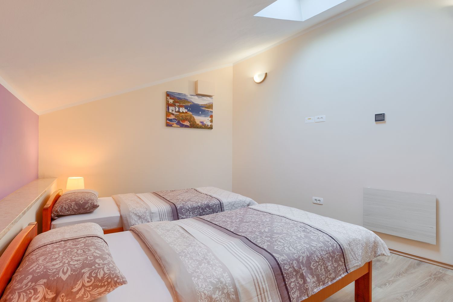 Ein Schlafzimmer mit zwei Betten, einem Bild an der Wand, einer Lampe und einem Oberlicht.