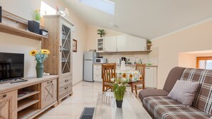 Un espace de vie compact comprenant un téléviseur, des meubles en bois, une table à manger avec des chaises, un canapé et un coin cuisine avec des placards et des appareils électroménagers.