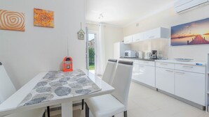 Une cuisine moderne avec des meubles blancs, une table à manger recouverte d’une nappe à motifs et une vue sur l’extérieur.