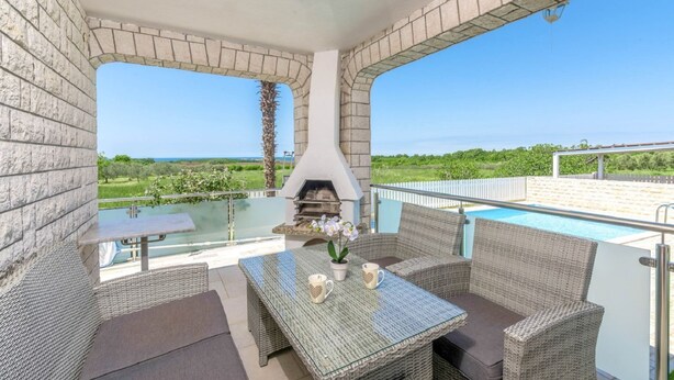 Un espace extérieur abrité comprenant une piscine, des meubles en osier et un barbecue.