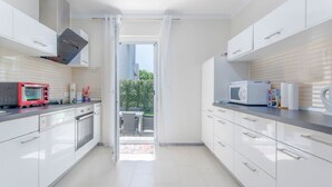 Une cuisine moderne avec des meubles blancs, un grille-pain rouge, un four à micro-ondes blanc et une vue sur une terrasse extérieure.