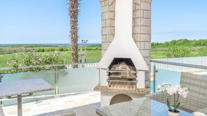Un barbecue en pierre installé sous une terrasse couverte, avec vue sur la mer.