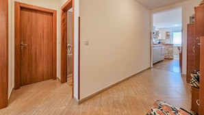 Ein Korridor mit Holztüren, einem Fliesenboden und Blick in einen Küchenbereich.