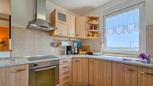 Eine moderne Küche mit Holzausstattung, einer Edelstahl-Dunstabzugshaube, einem Fenster mit Blick und einer gefliesten Spritzschutzwand.