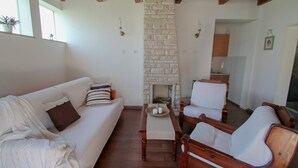 Ein Wohnzimmer mit einem weißen Sofa, einem Holztisch und zwei Holzstühlen. In der Mitte befindet sich ein Kamin aus Backsteinen.
