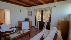 Ein gemütliches Zimmer mit Holzbalkendecke, einem Bett, einem Sofa, einem Schreibtisch mit Computer und einem fenster mit Vorhängen.
