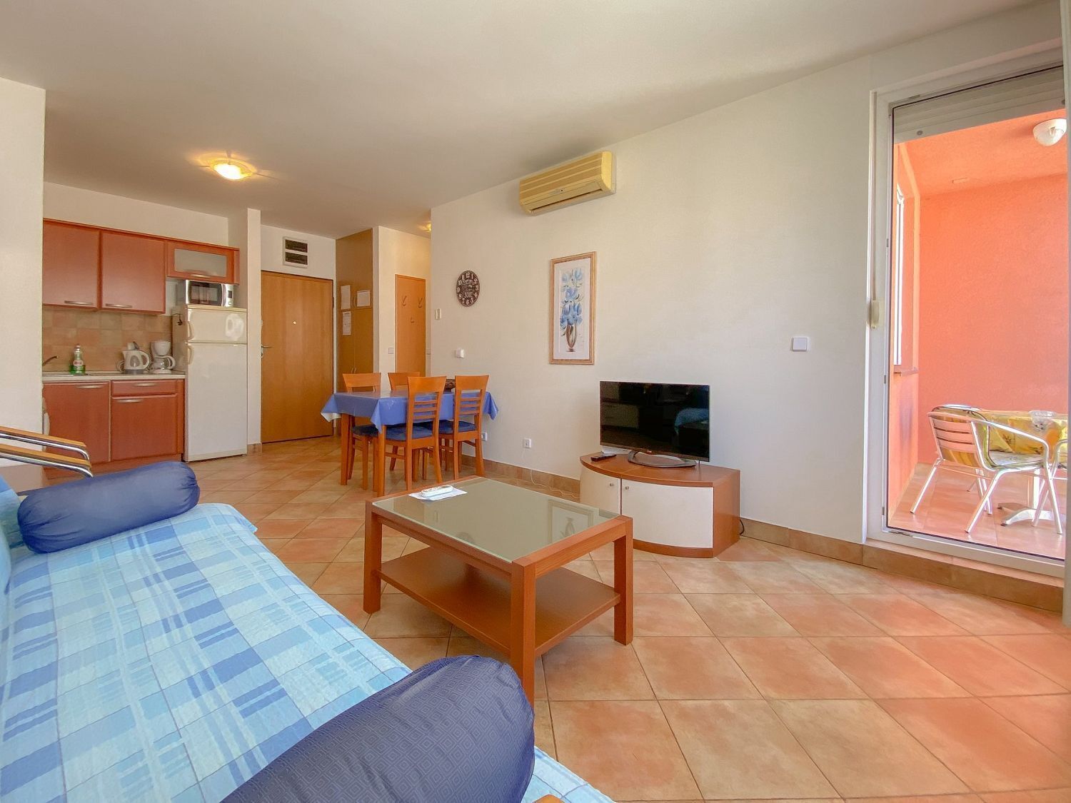 A compact living space with a sofa, a dining table with chairs, a TV, and a kitchen area.