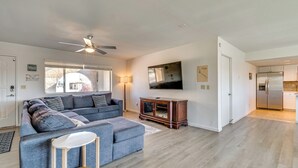 Ein modernes Wohnzimmer mit einem grauen Ecksofa, einem Holzschrank und einem Deckenventilator.
