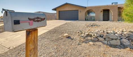 A mailbox with a Harley-Davidson logo, a house with a garage, and a gravel driveway.
