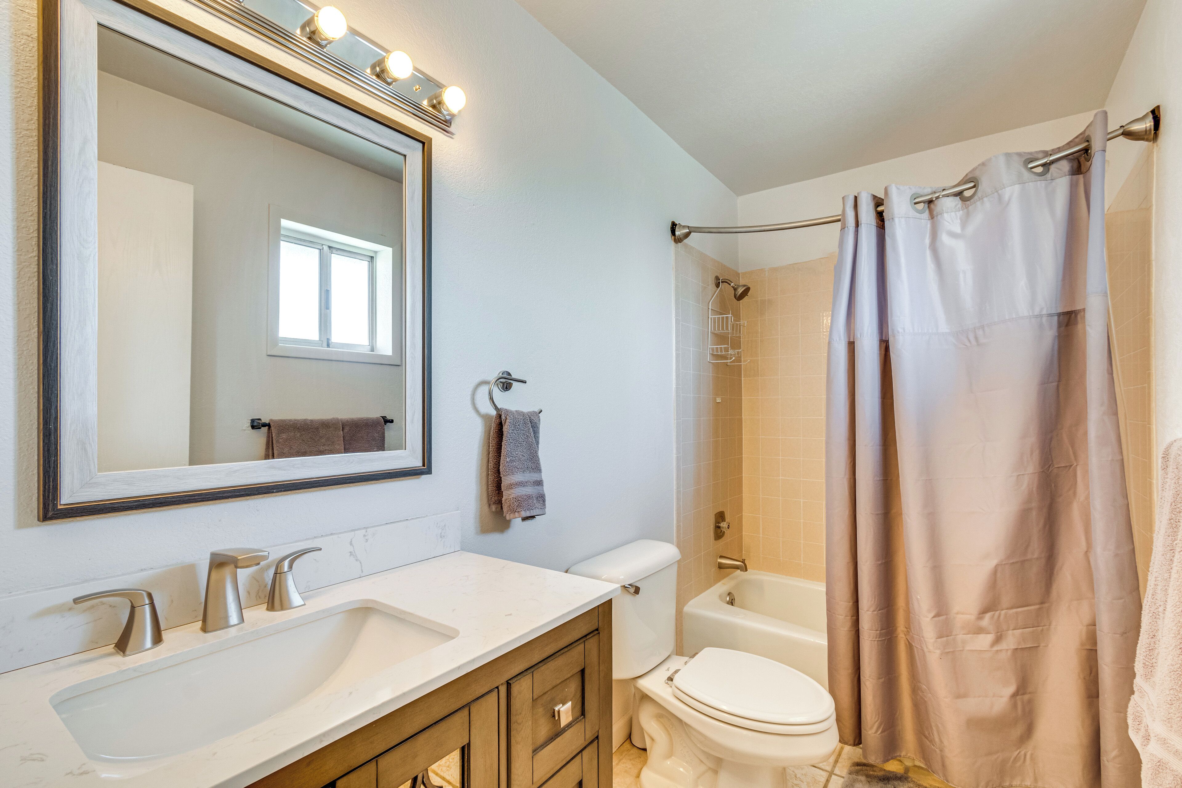 Un baño con lavamanos blanco, espejo, inodoro y cortina de ducha.