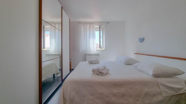 A hotel room with a large bed, a mirror, a window with curtains, and a radiator.