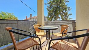 An outdoor seating area with wicker chairs and a small round table, overlooking a garden and a building with a tiled roof. - Comfortable, dog-friendly apartment with private balcony, washing machine, WiFi (Novigrad)