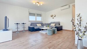 Ein modernes Wohnzimmer mit einer grauen Eckcouch, einem weißen Couchtisch und zwei Barhocker.