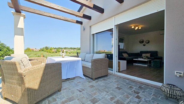 Eine Terrasse im Freien mit Korbmöbeln, einem Tisch mit weißer Tischdecke und einer Glasschiebetür zu einem Wohnbereich mit einer Couch und einem Couchtisch.