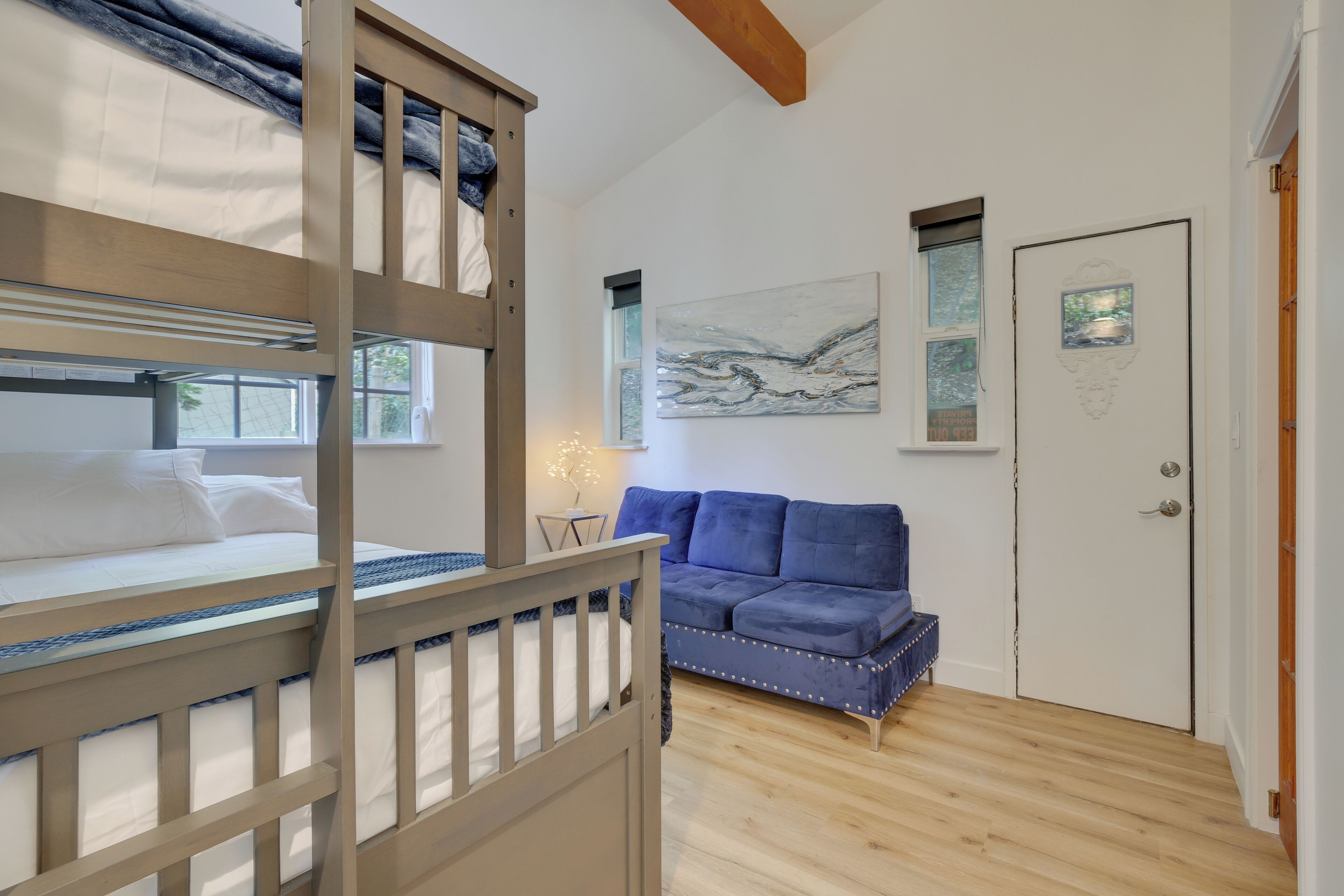A room with a bunk bed, a blue sofa, a door with a picture, and a window with a view.