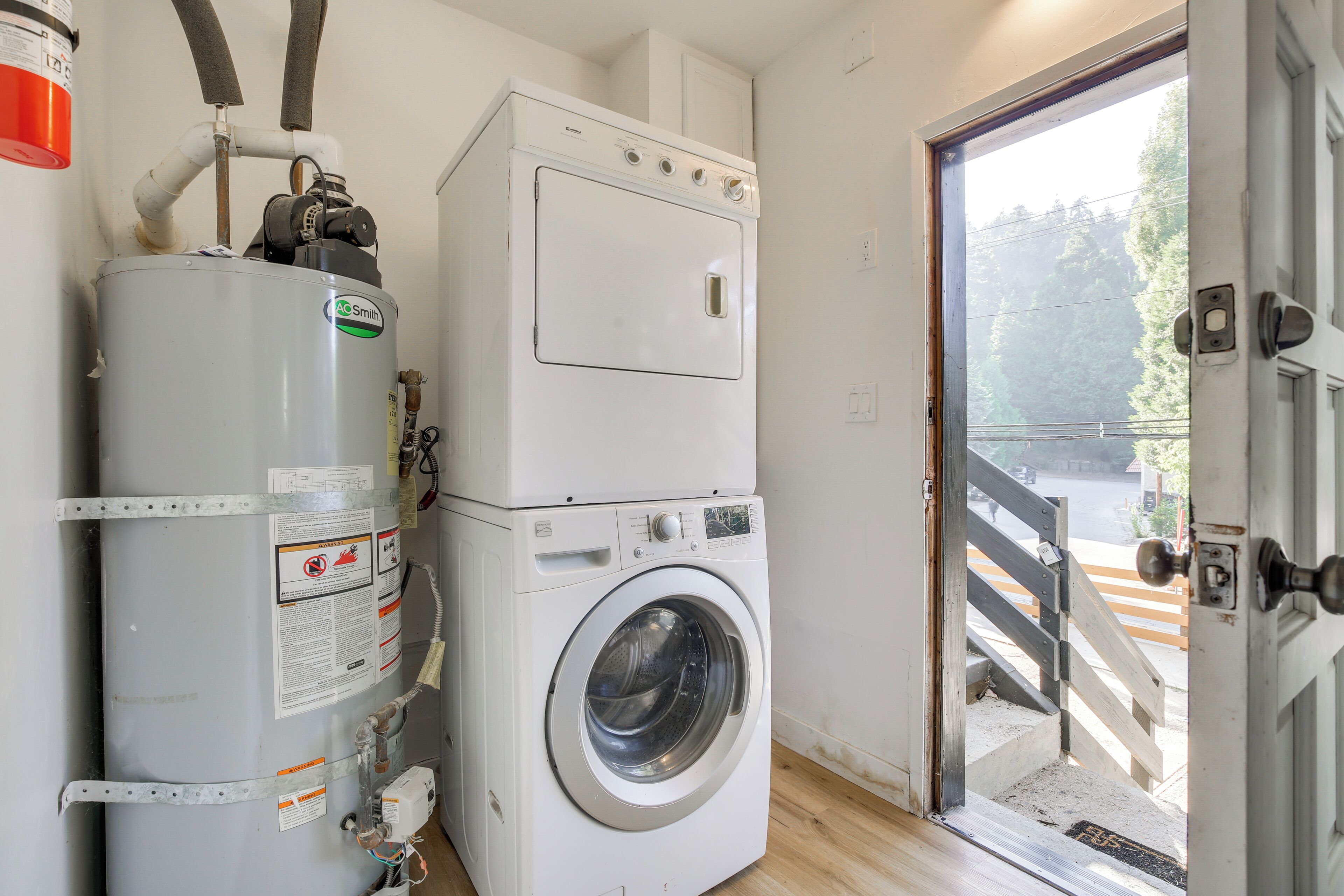 A laundry room with a stacked washer and dryer, a water heater, and a door leading outside.