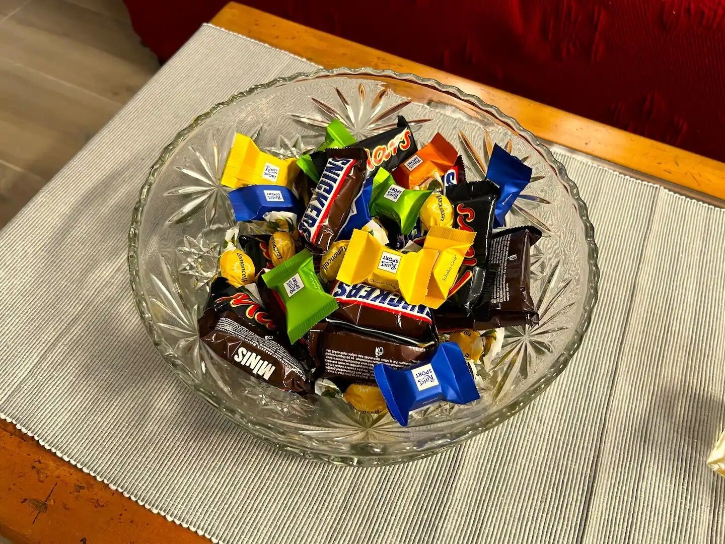 Un cuenco de vidrio lleno de diversas barras de chocolate sobre un posavasos con textura.