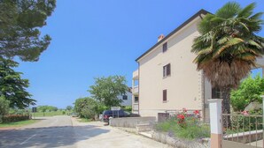 A two-story building with a beige facade, a visible balcony, and a palm tree in the foreground. - Charming apartment only 250 meters to the beach with WiFi, BBQ, private parking (Novigrad)