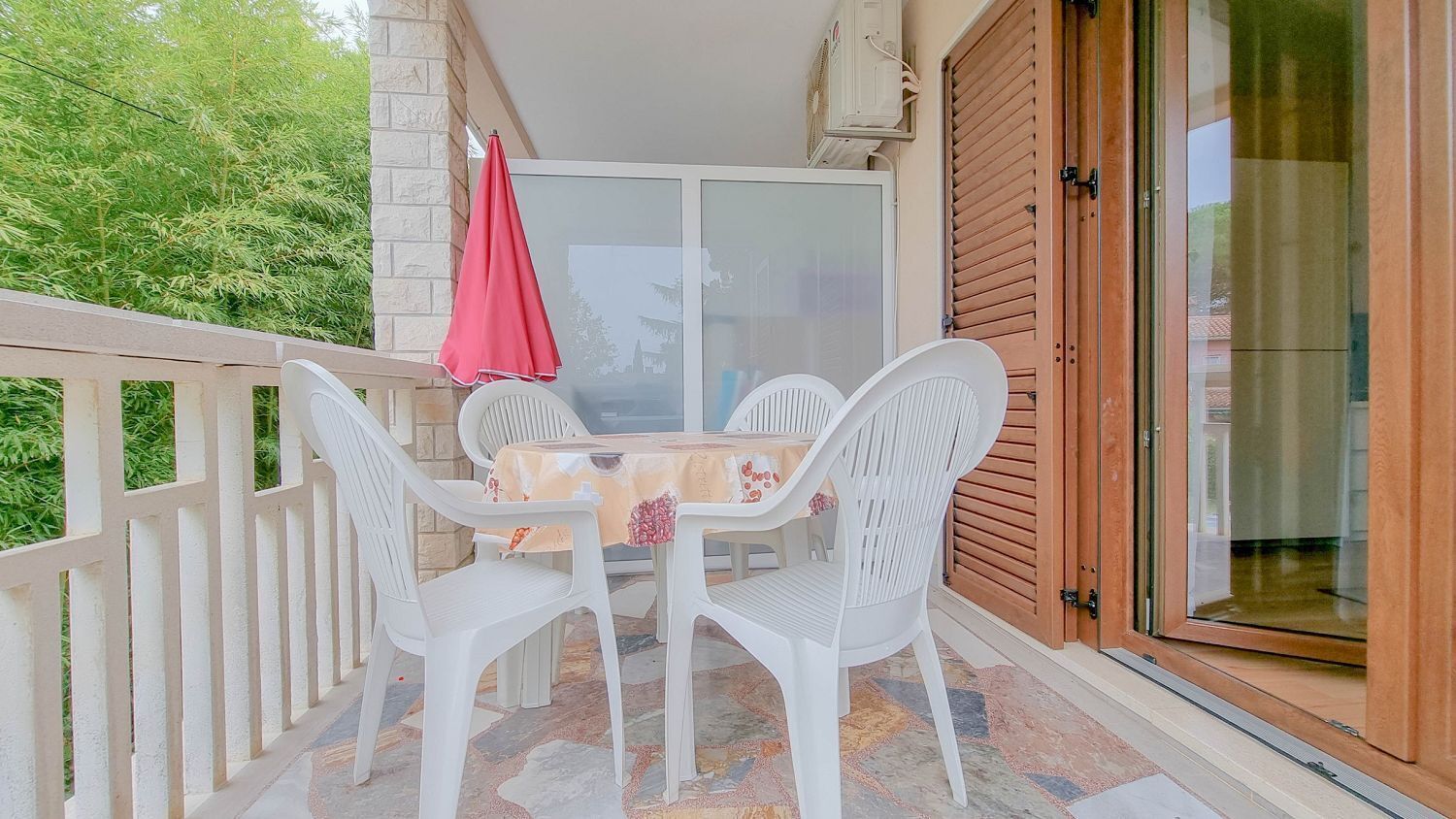 Ein Balkon mit Tisch und Stühlen, einem roten Sonnenschirm und einer Schiebeglastür.