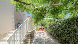 A stone staircase leading to a covered outdoor area with a white railing, surrounded by greenery and a tiled floor. - Charming apartment only 250 meters to the beach with WiFi, BBQ, private parking (Novigrad)