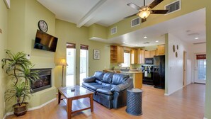 A spacious living room with a leather sofa, wooden coffee table, and a potted plant. A television is mounted on the wall, and there is a ceiling fan overhead.