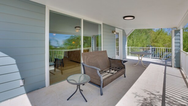 A covered outdoor seating area with a cushioned bench and a small table, connected to a building with light blue siding.