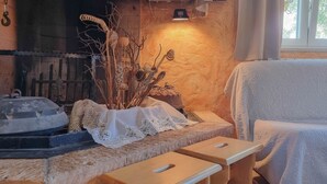 A cozy room with a stone fireplace, a lace-covered table, and a cushioned chair. - Mediterranean studio apartment with sunbathing lawn, barbecue area and dog-friendly (Novigrad)