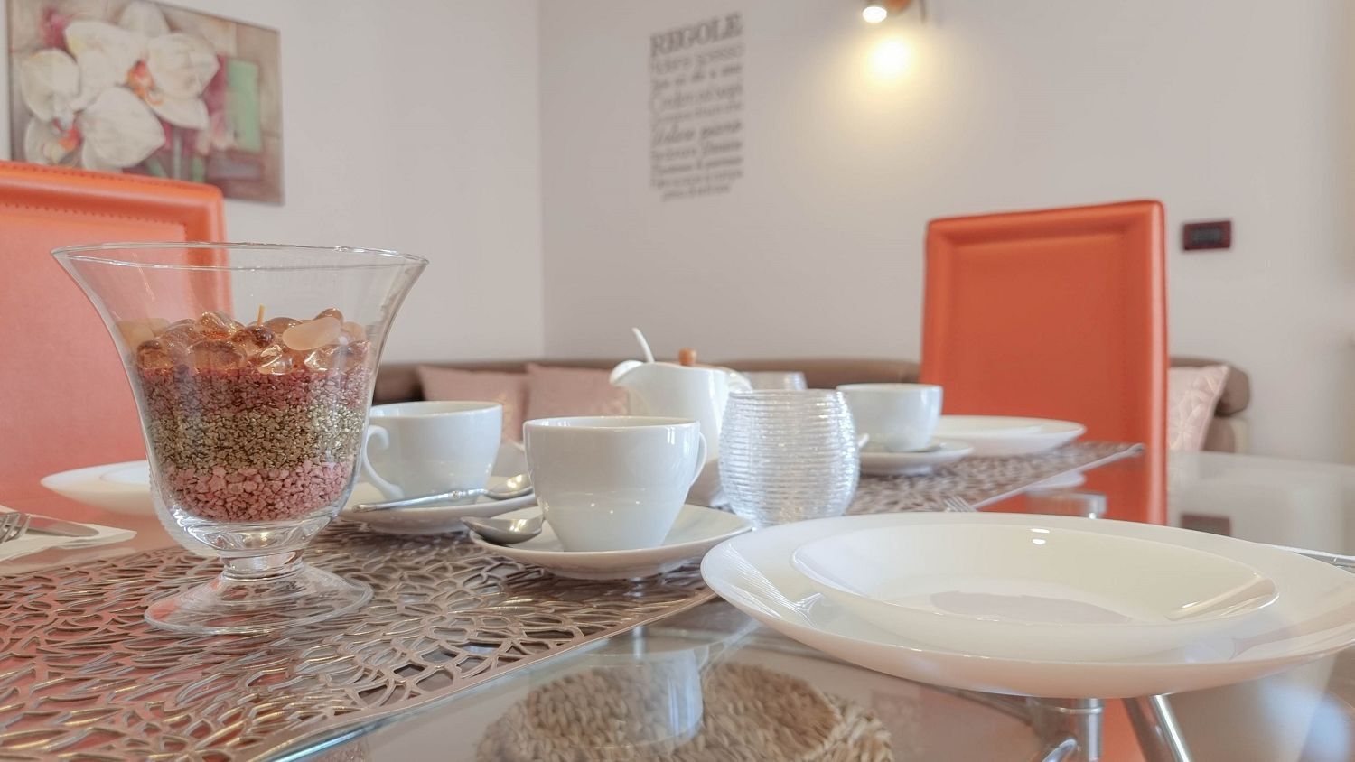 A dining area with a glass table, white plates, and a clear glass with a mix of items.