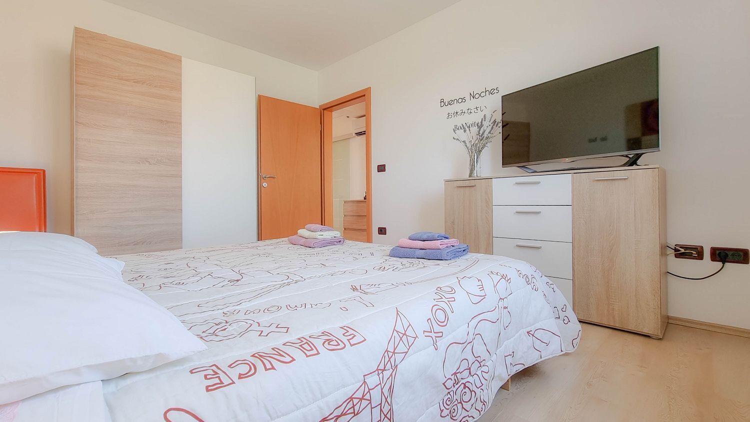 A bedroom with a bed, a TV, a wardrobe, and a door leading to another room.
