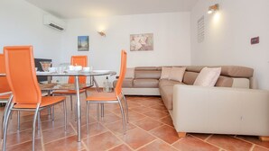 A dining area with orange chairs, a round table, and a beige sofa. - Bright apartment with sea view, sunbathing lawn, barbecue area, washing machine (Novigrad)