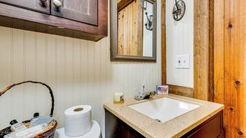 A bathroom with a wooden vanity, a sink, a mirror, and a toilet.