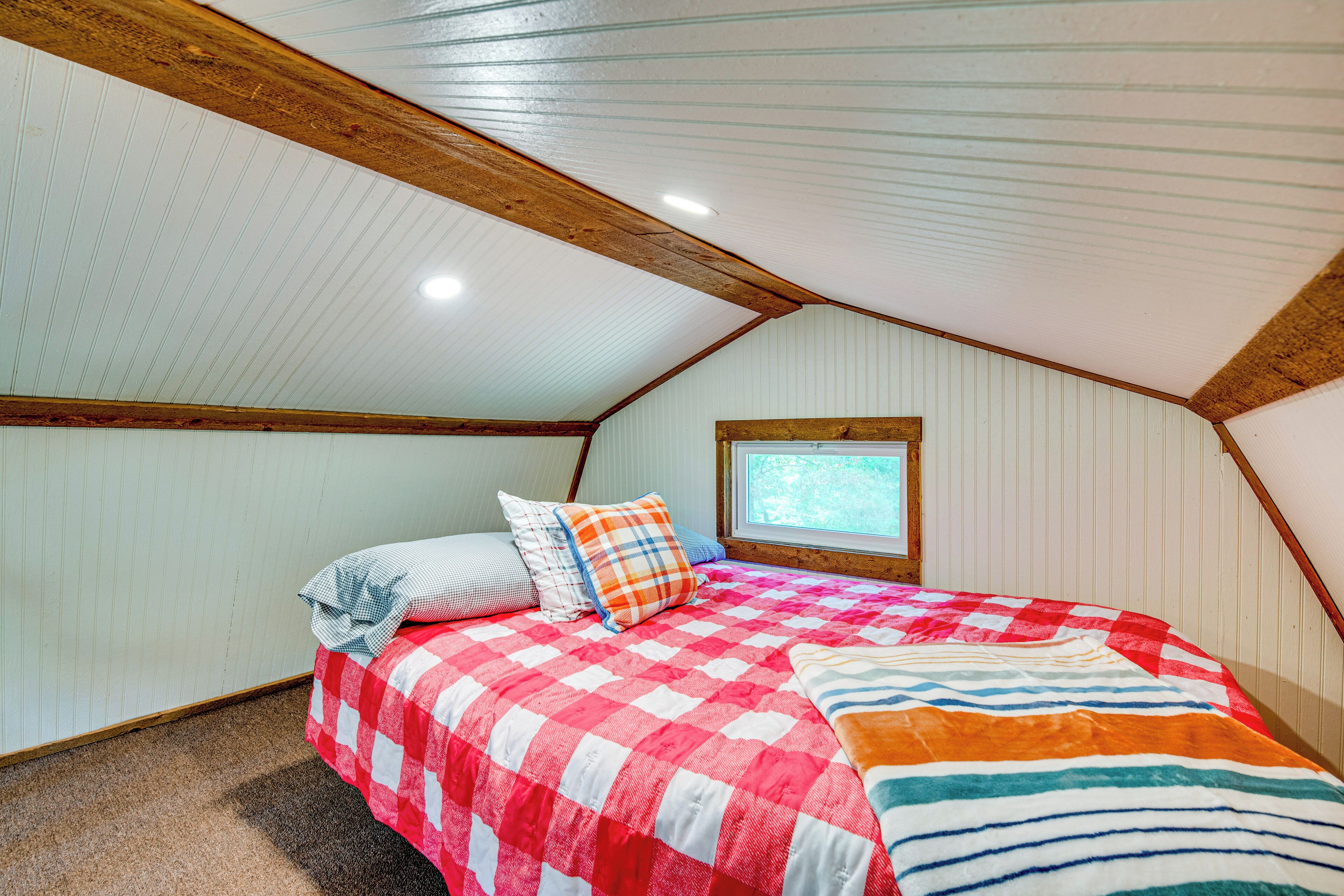 A bedroom with a checkered bedspread, a window with a view, and wooden beams on the ceiling.