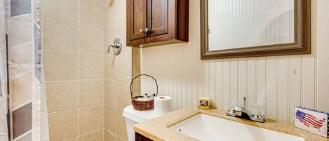 A bathroom with a beige tiled shower, a wooden cabinet, a sink with a mirror above it, and a small American flag decoration.